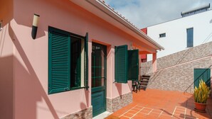 A pink building with green shutters, a tiled patio, and a staircase leading to a white building. - GuestReady - Serene Paradise in Machico (Machico)