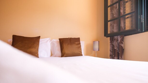 A neatly made bed with white and brown pillows, a lamp, and a window with curtains. - GuestReady - Serene Paradise in Machico (Machico)