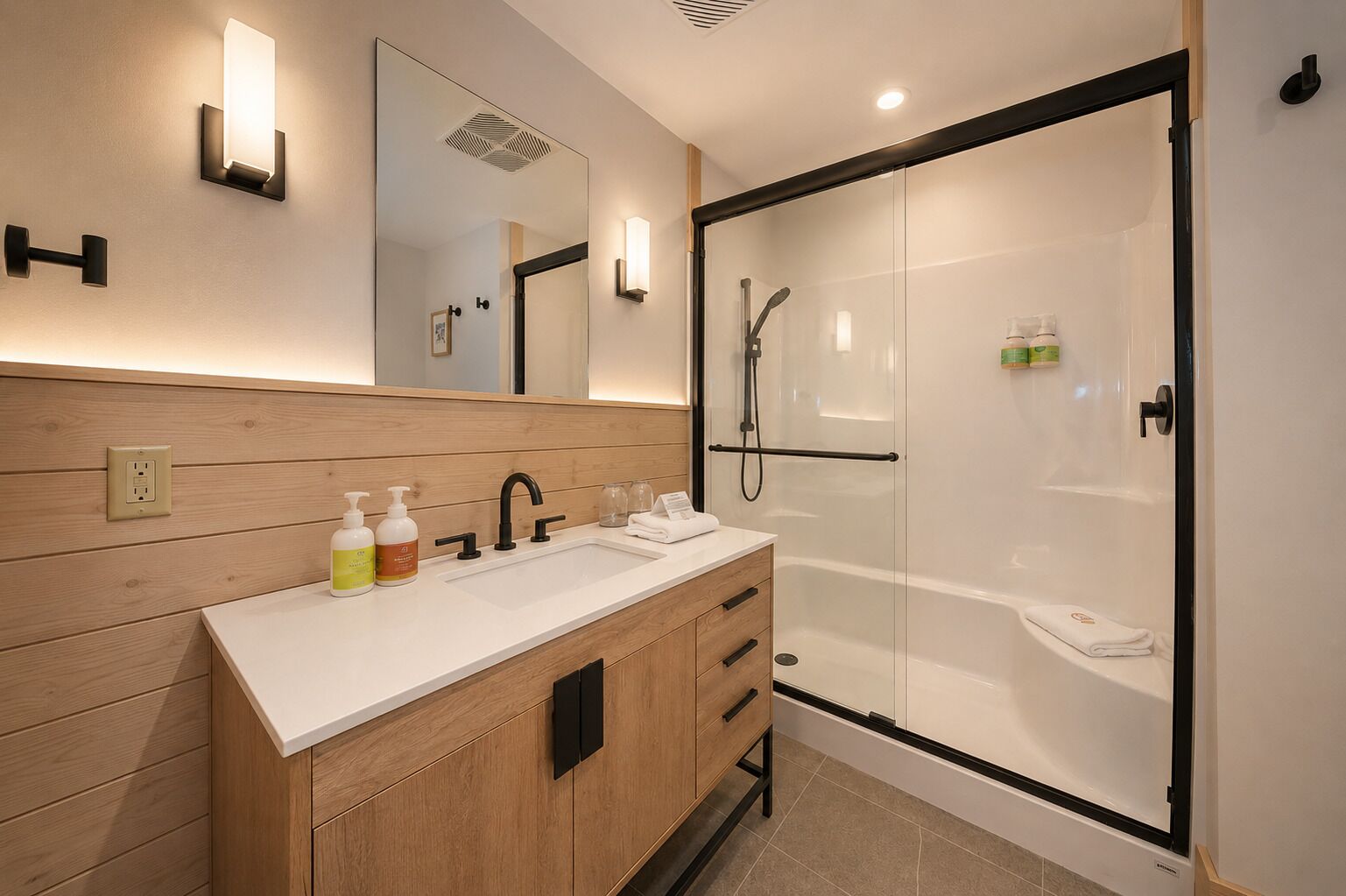 A modern bathroom with a wooden vanity, a glass-enclosed shower, and wall-mounted lighting.