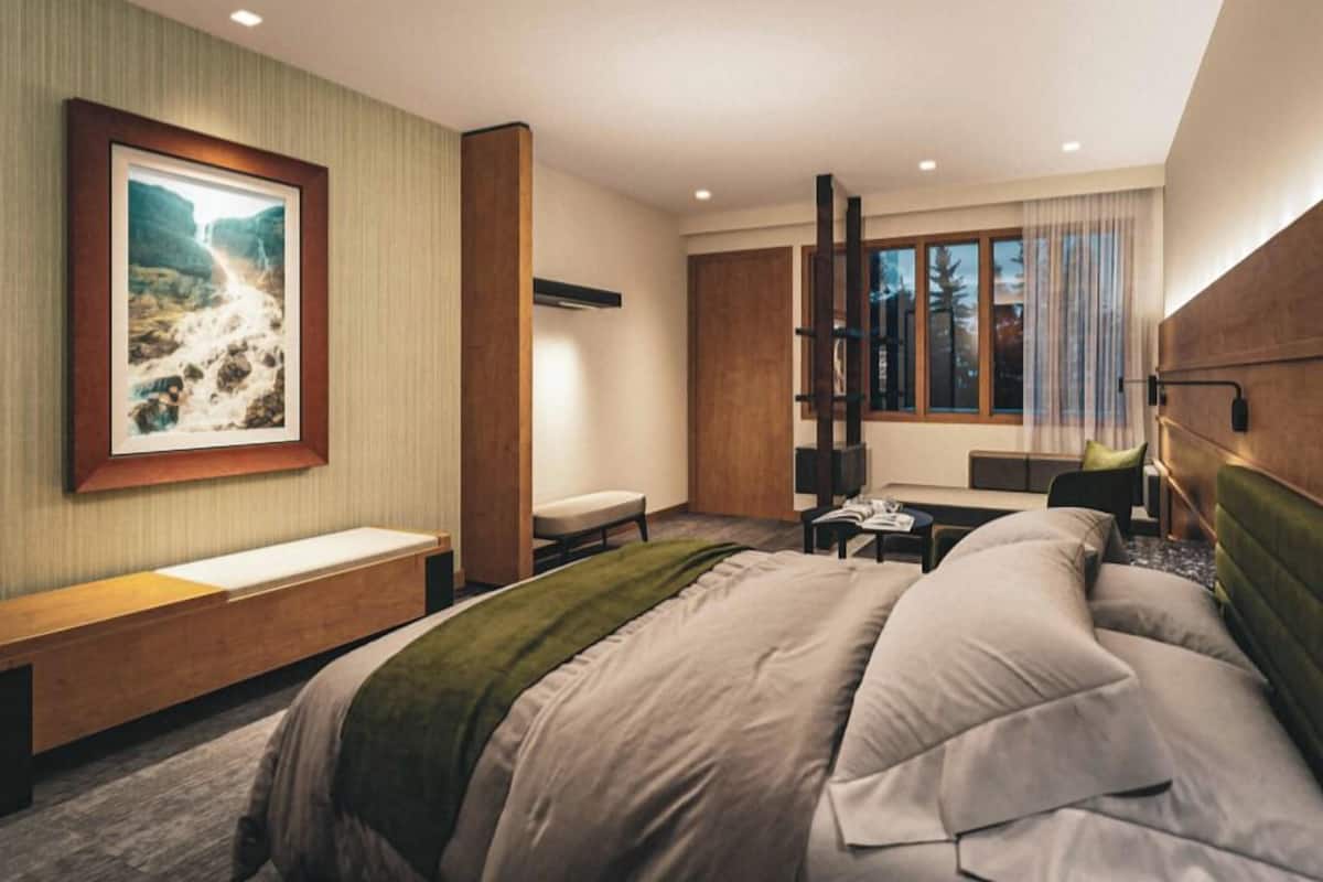 Una habitación de hotel moderna con una cama grande, un banco, un escritorio y una ventana con cortinas.