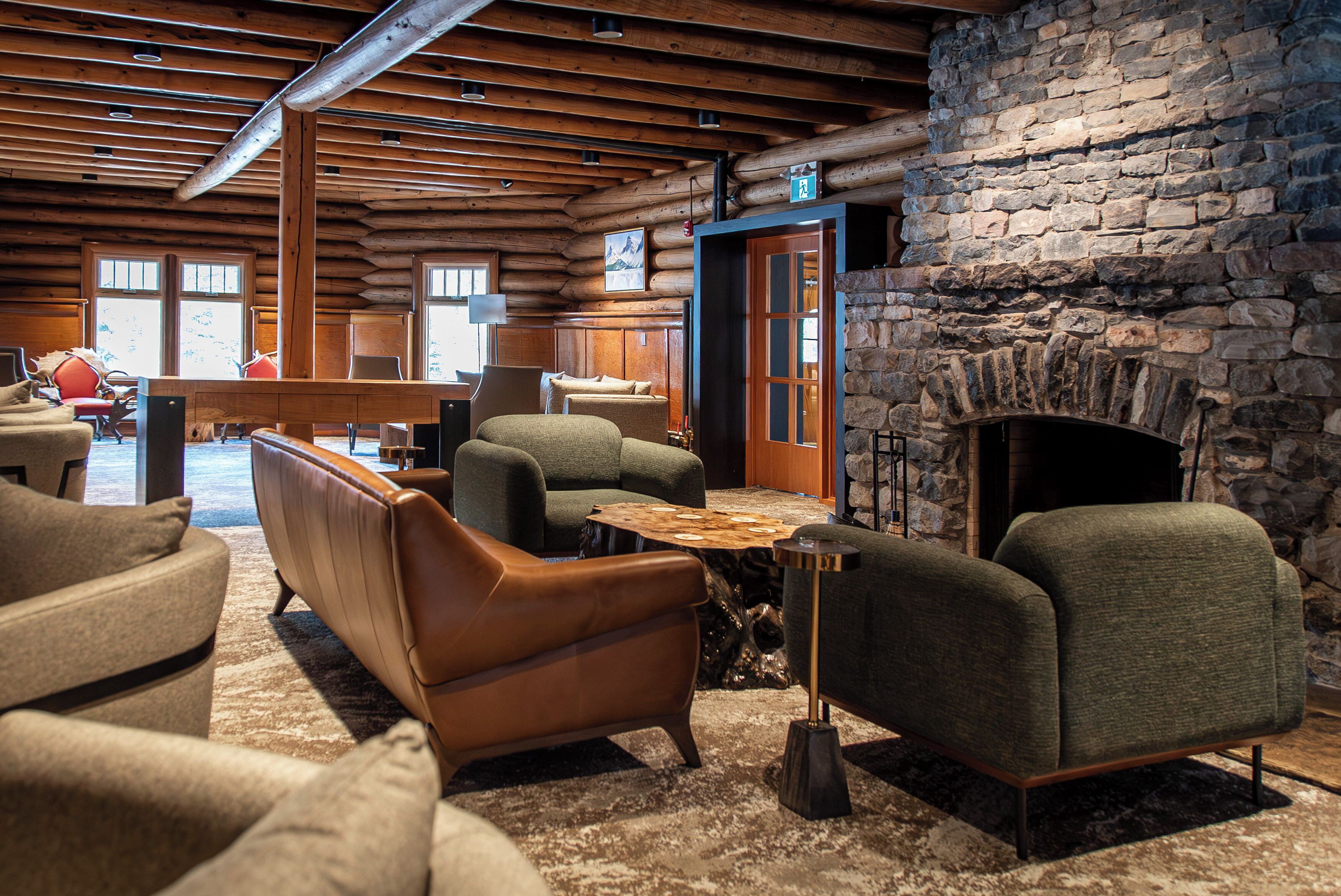 A log cabin interior with a stone fireplace, wooden ceiling beams, and multiple seating areas.