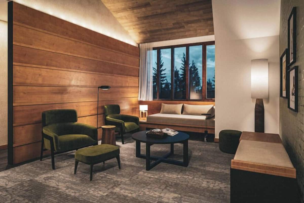 Una habitación con pared de paneles de madera, un sofá, dos sillones, una mesa de centro, una lámpara y una ventana con vistas a árboles.