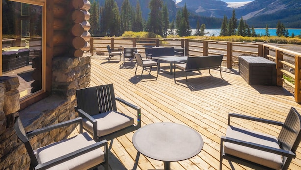Una terraza de madera con mobiliario exterior, un muro de piedra y vistas a montañas y un lago.