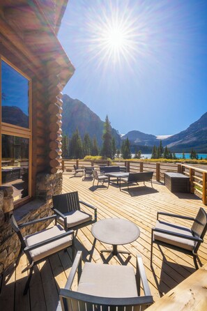 A wooden deck with outdoor furniture, a stone wall, and a view of mountains and a lake.