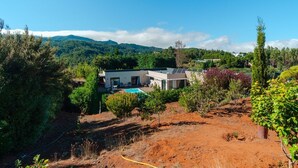 Una casa moderna con piscina, rodeada de exuberante vegetación y colinas.