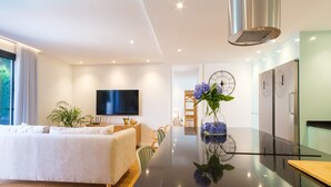 Una habitación de hotel moderna con una cama grande, un televisor de pantalla plana, una zona de comedor con mesa de cristal y un reloj de pared.