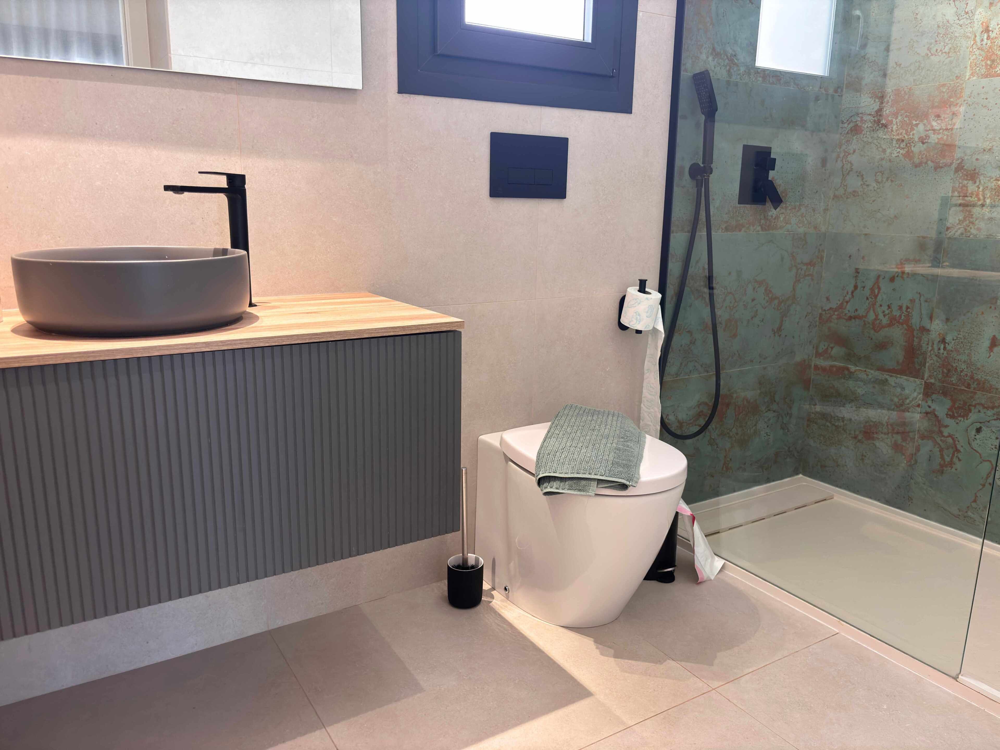 A modern bathroom with a vessel sink, toilet, and glass shower enclosure.