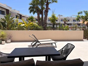 An outdoor patio with a table and chairs, surrounded by potted plants and palm trees.