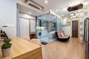 Cozy living space with a dining table, sofa, and chair, featuring a compact kitchenette with a washing machine and sink.