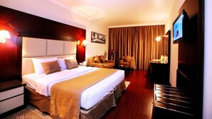 Quarto de hotel com uma cama grande, uma escrivaninha, uma cadeira, uma televisão e uma janela com cortinas.