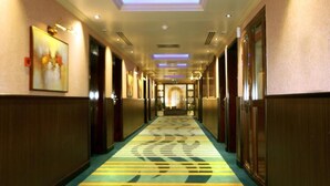 Corredor de hotel com carpete estampado, painéis de madeira e teto com iluminação embutida.