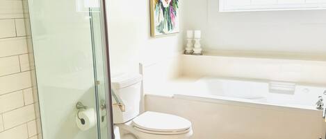 A bathroom with a glass shower enclosure, a toilet, a bathtub, and a sink.
