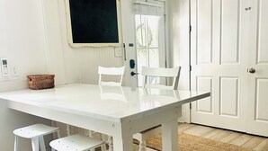 Una mesa de comedor blanca con dos taburetes, una silla blanca y una cesta tejida en el suelo.