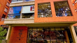 A multi-story building with a brick facade, large windows, and a ground-level entrance with a sign. - Bright Studio with Balcony 615 (Bogotá)