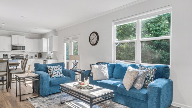 A modern living room with a blue sofa set, a coffee table, and a view of the outdoors through large windows. - Luxury 5BR Ideal For Vacationers, Groups, Corporate & Insurance Stays Near ATL (Fairburn)