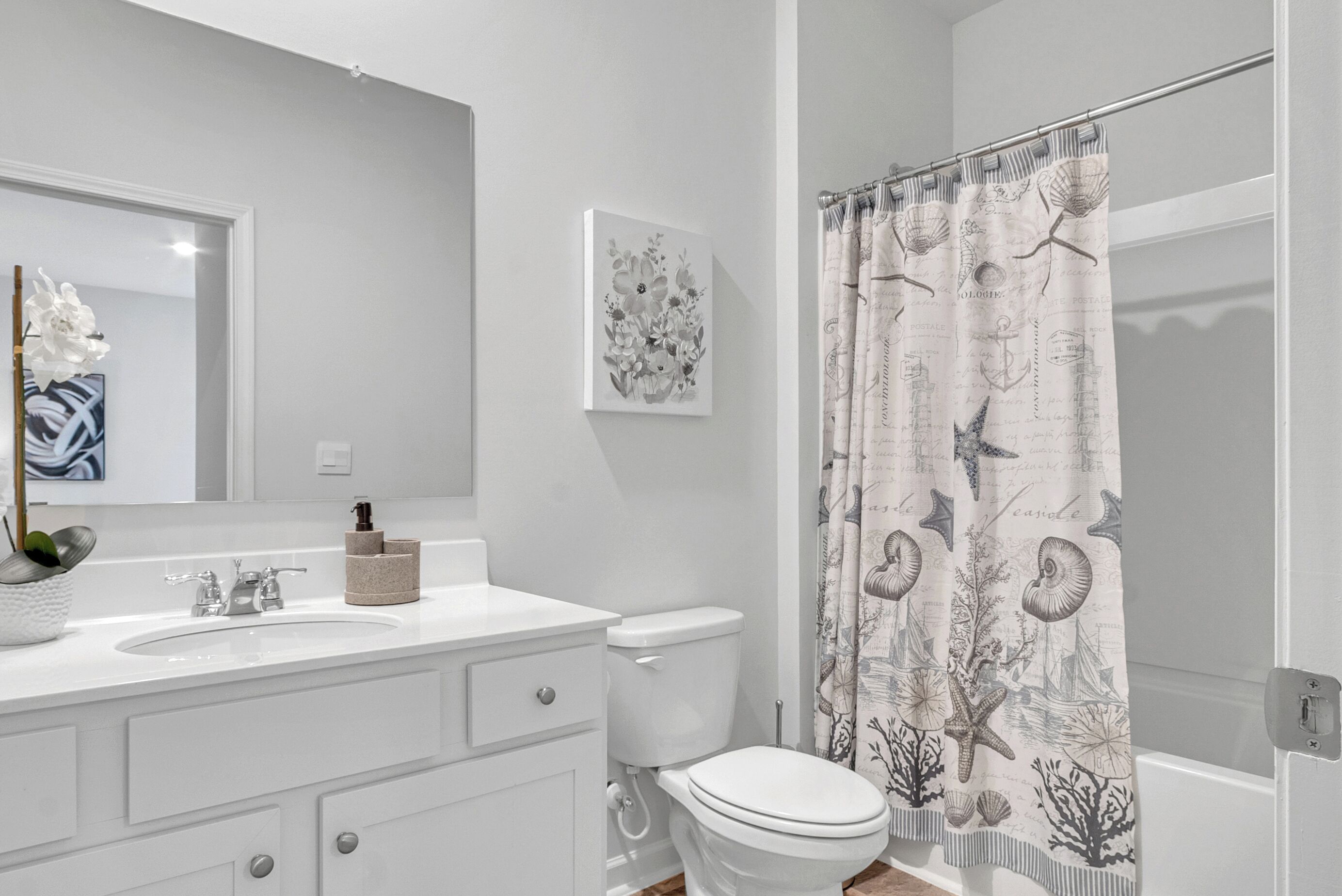 A bathroom with a white sink, a toilet, a mirror, and a shower curtain with a nautical theme.