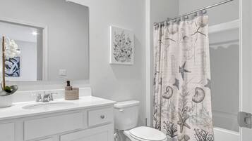 A bathroom with a white sink, a toilet, a mirror, and a shower curtain with a nautical theme.
