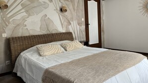 Een slaapkamer met een groot bed, een geweven hoofdeinde en een muur met een bladmotief.