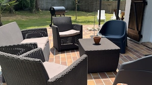 Een terras met wicker meubels, een barbecue en een overdekte zithoek.