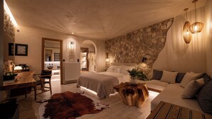 Ein Schlafzimmer mit Steinwand, einem Holztisch, einem Kuhfellteppich und einem Bett mit Kopfteil.