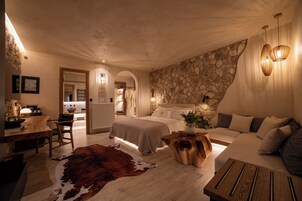 A bedroom with a stone wall, a wooden dining table, a cowhide rug, and a bed with a headboard.