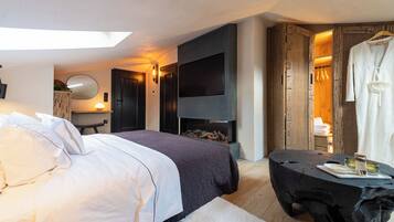 A modern hotel room with a large bed, a flat-screen TV, a fireplace, and a wooden wardrobe.