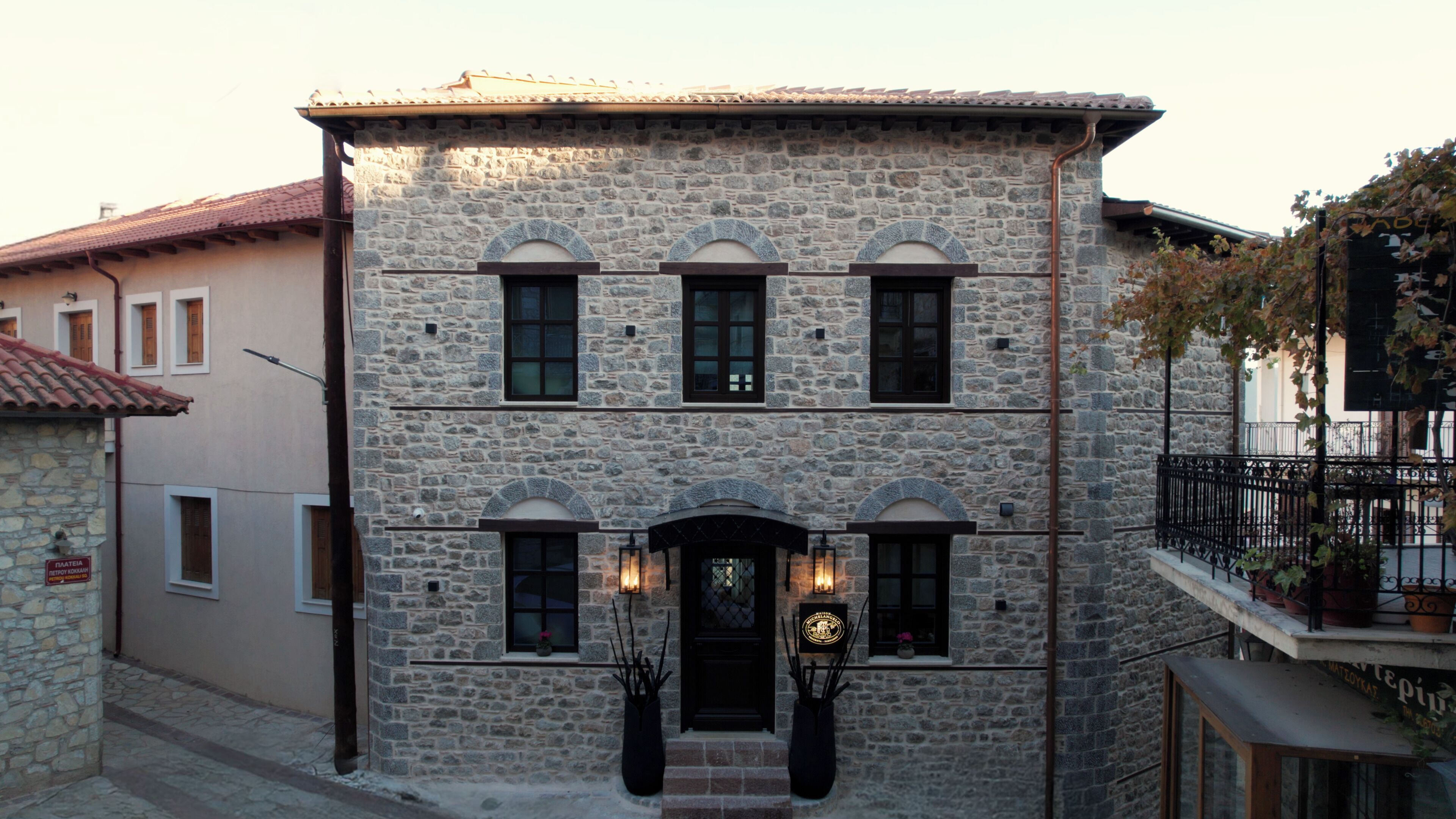A stone building with a central entrance, multiple windows, and a balcony with potted plants.