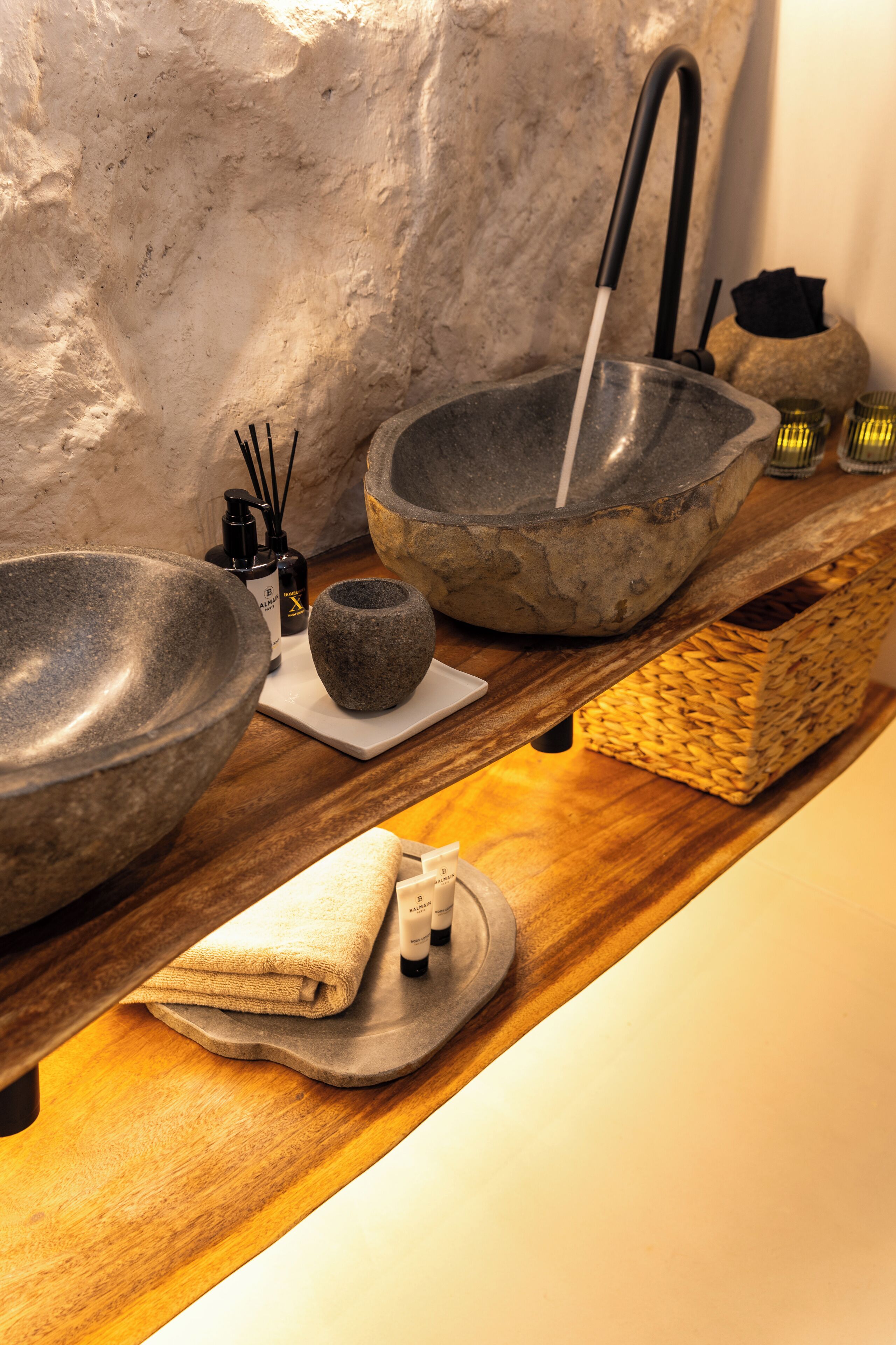 A bathroom with a stone sink, a wooden shelf with toiletries, and a textured wall.