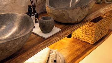 A bathroom with a stone sink, a wooden shelf with toiletries, and a textured wall.