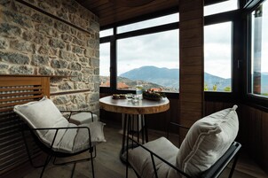 Una habitación acogedora con paredes de piedra, una mesa redonda de madera con vistas a las montañas, dos sillas con cojines y un banco de madera.