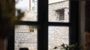 A view through a window with a stone wall and a window with a metal grille.
