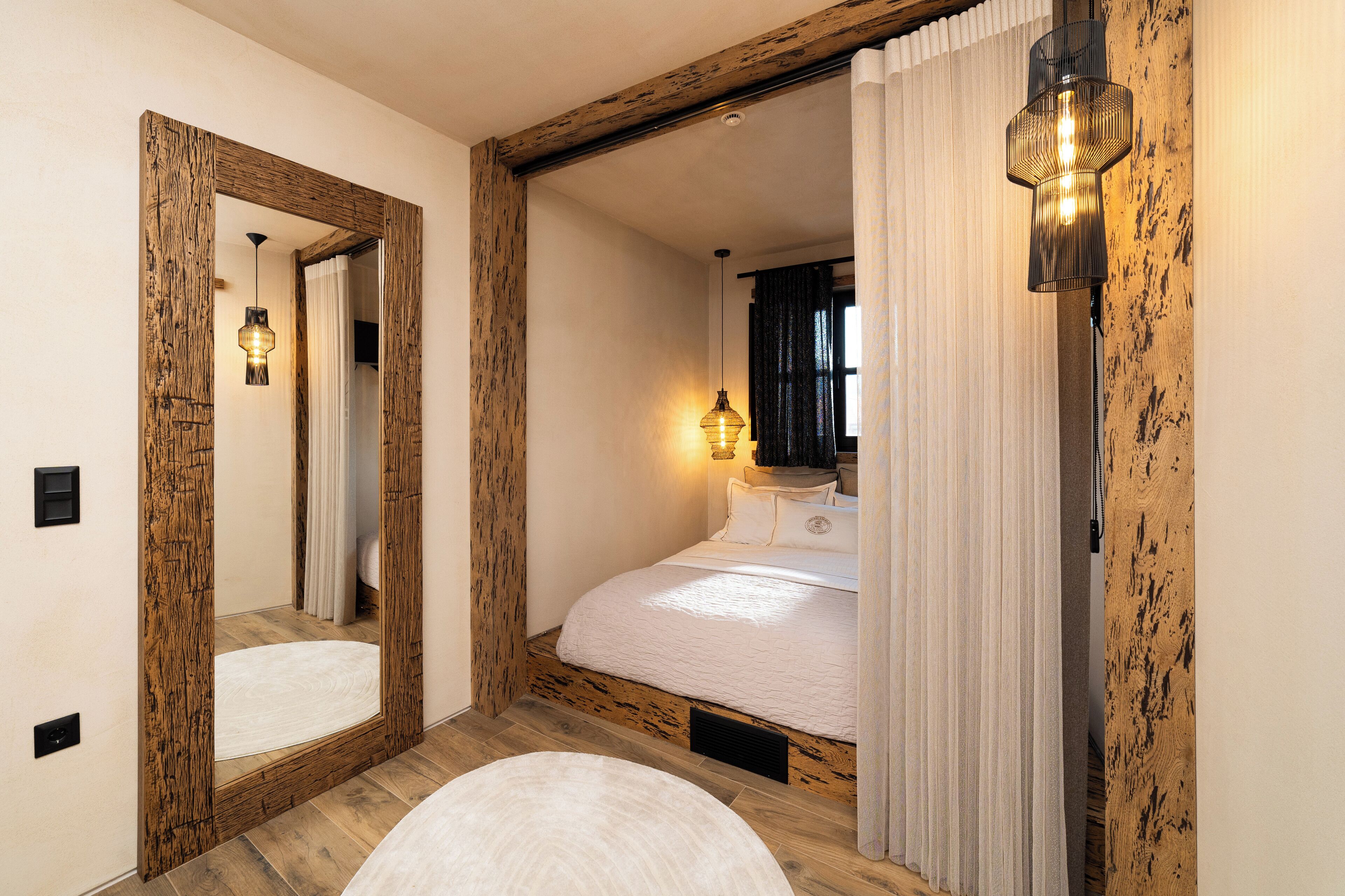 A bedroom with a large mirror, wooden beams, a bed with white bedding, and a wall-mounted light fixture.