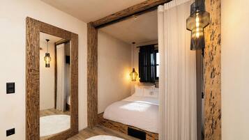 A bedroom with a large mirror, wooden beams, a bed with white bedding, and a wall-mounted light fixture.