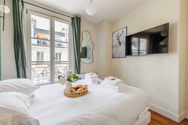 A hotel room with a bed, a TV, a window with curtains, a mirror, and a wall-mounted picture.