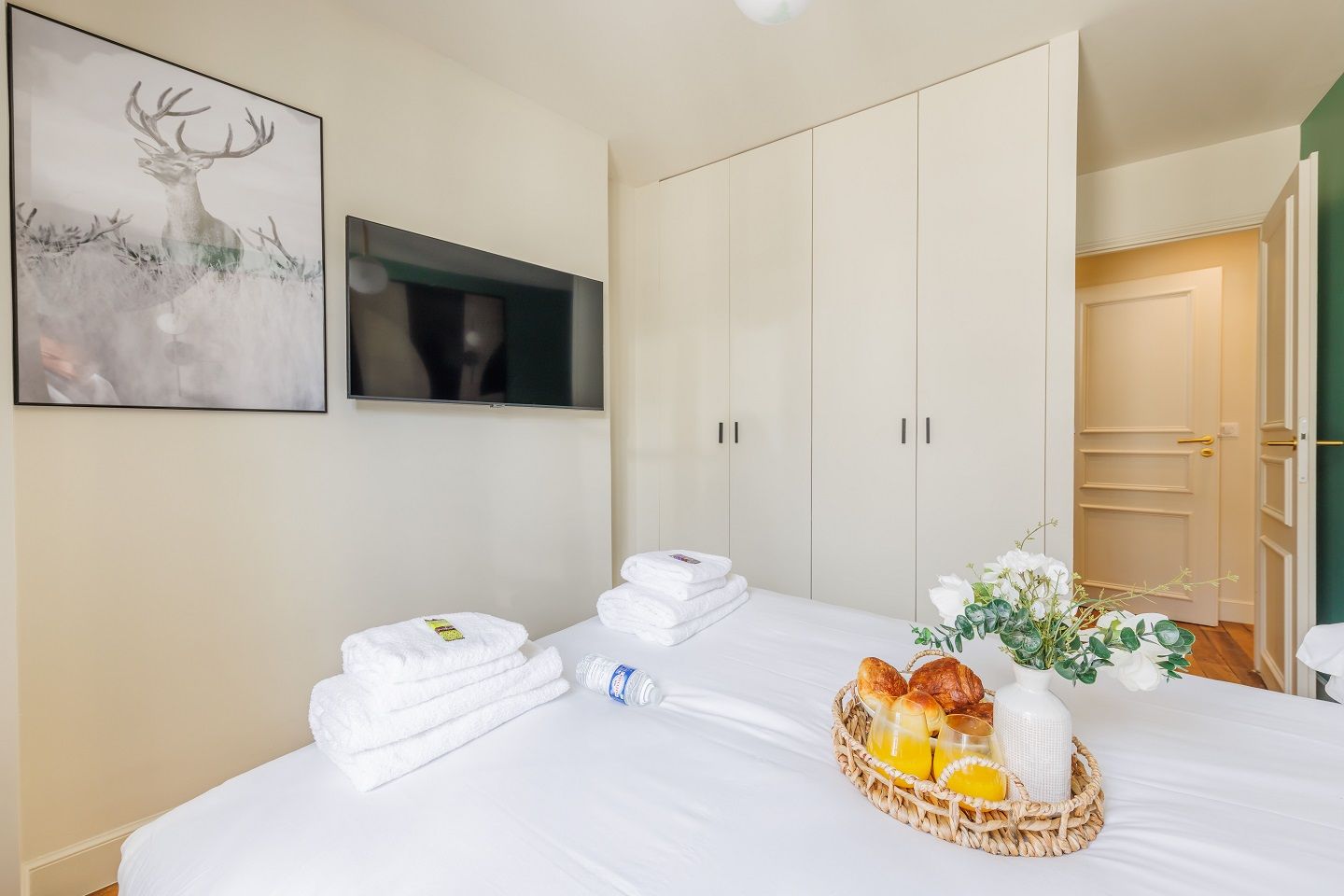 Et hotelværelse med seng, fladskærms-tv, et billede af et rådyr, en bakke med morgenmad og en dør, der fører til et andet rum.