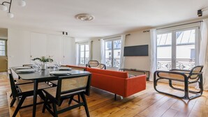 A modern living room with a dining table set for four, a sofa, a chair, and a TV on the wall. - Authentic Parisian Elegance in the Heart of the 6th Arrondissement (Paris)