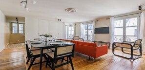 Un soggiorno moderno con un tavolo da pranzo apparecchiato per quattro persone, un divano, una poltrona e una TV appesa al muro.