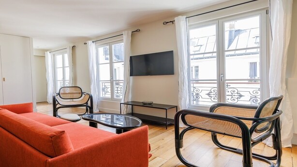 A modern living room with a sofa, two chairs, a small table, and a TV on the wall. - Authentic Parisian Elegance in the Heart of the 6th Arrondissement (Paris)