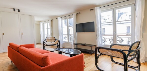 Una sala de estar moderna con un sofá, dos sillones, una mesita y un televisor en la pared.