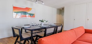Zona pranzo con tavolo apparecchiato per quattro persone, sedie e un quadro appeso al muro.