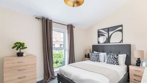 Un dormitorio moderno con una cama grande, una mesita de noche, un aparador y una ventana con cortinas.
