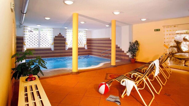 An indoor swimming pool with a sun terrace, lounge chairs, and a staircase leading to a higher level.