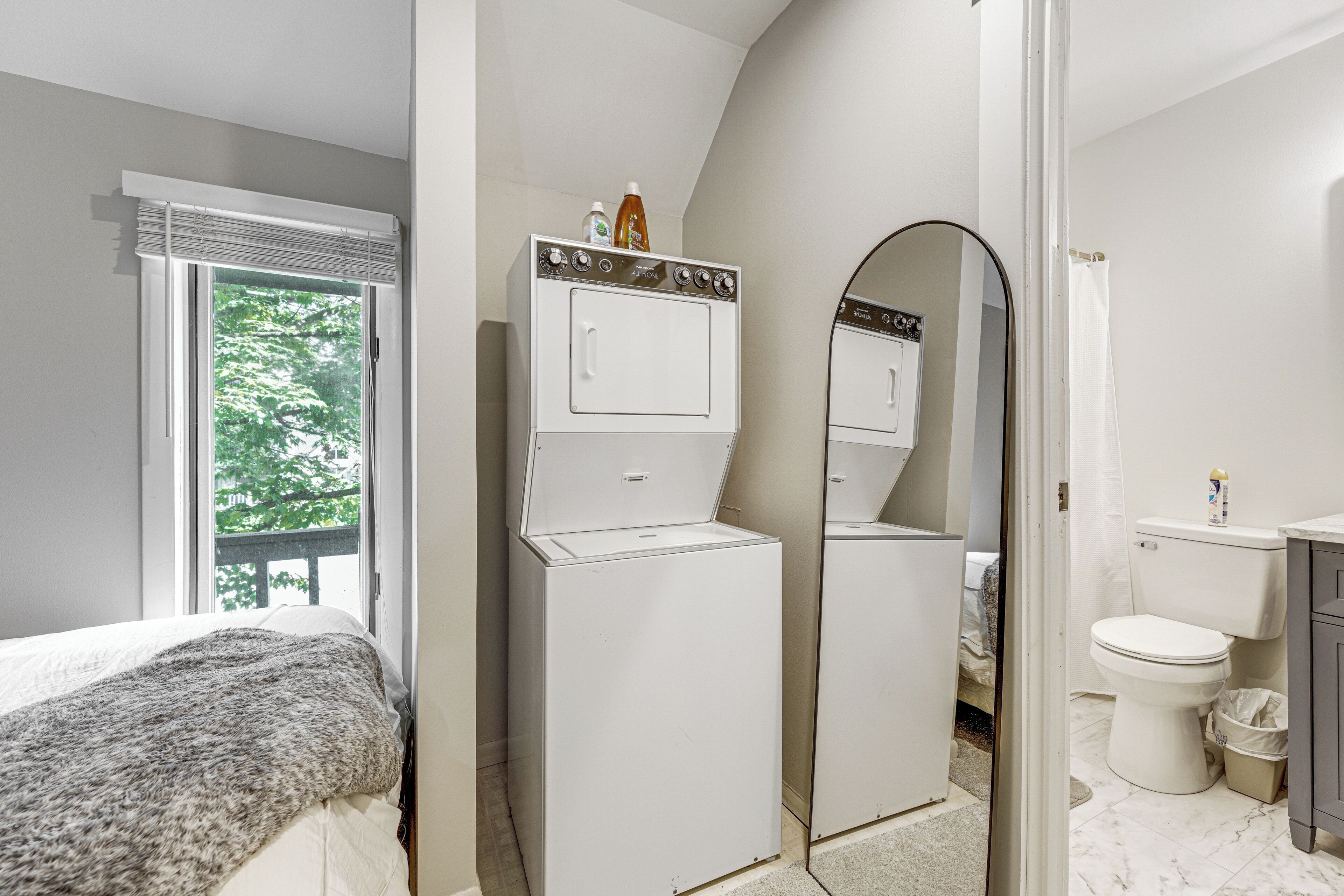 Un dormitorio con cama, lavadora, espejo y baño con inodoro y lavabo.