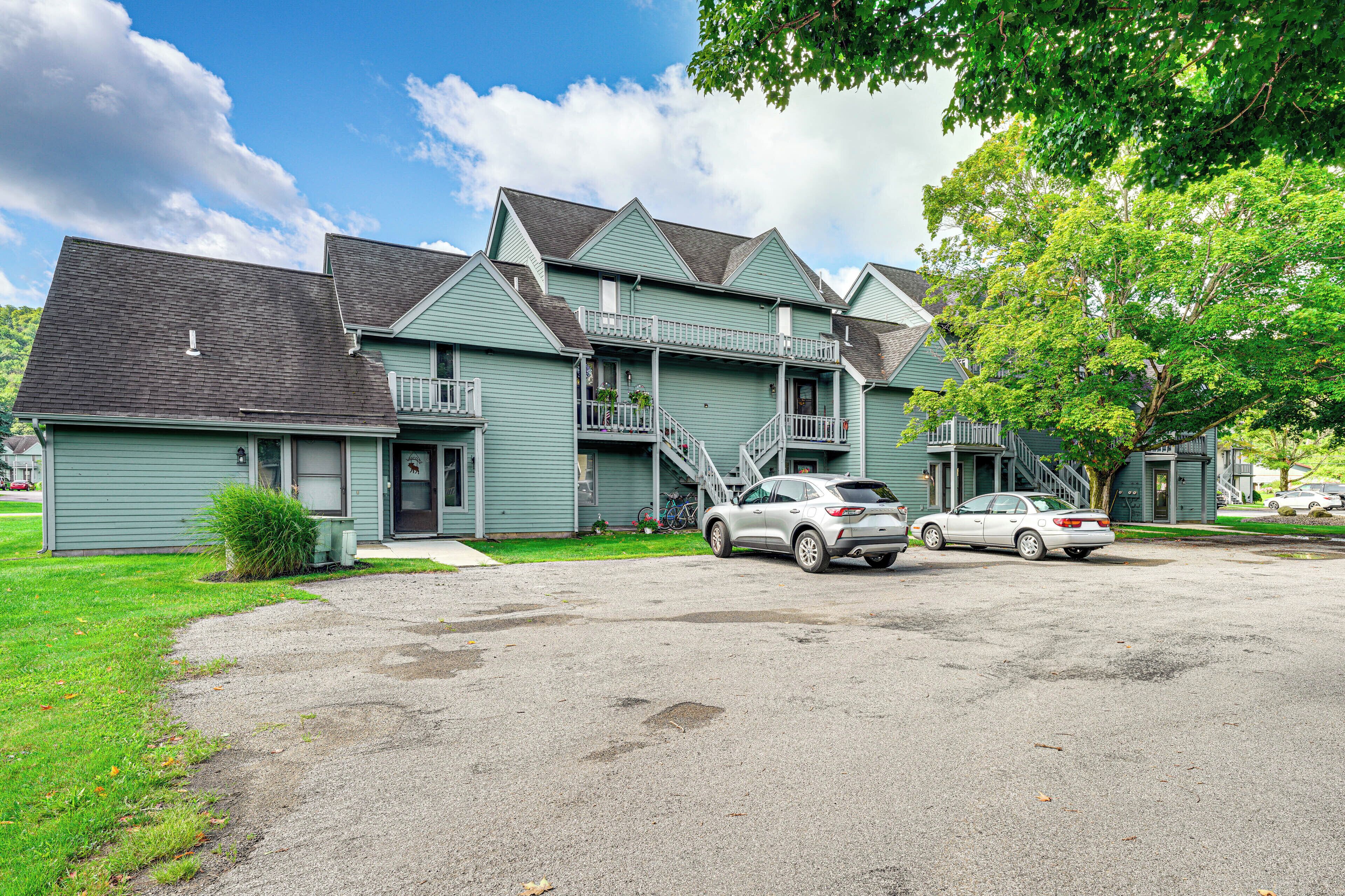 A two-story building with a front porch, a staircase leading to the second floor, and a driveway with two cars parked.