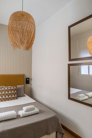 Une chambre d’hôtel avec un lit, un grand miroir et un luminaire suspendu.