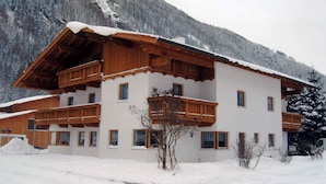 A multi-story chalet with wooden balconies and a snow-covered roof, surrounded by a mountainous landscape. - Holiday apartment with balcony (Längenfeld)
