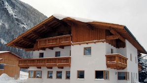 A multi-story wooden chalet with balconies, set against a snowy mountainous backdrop. - Holiday apartment with balcony (Längenfeld)