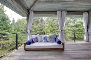 A wooden deck with a bed and white curtains, overlooking a forested area. - Serene Washington Island Getaway w/ Private Beach! (Washington Island)