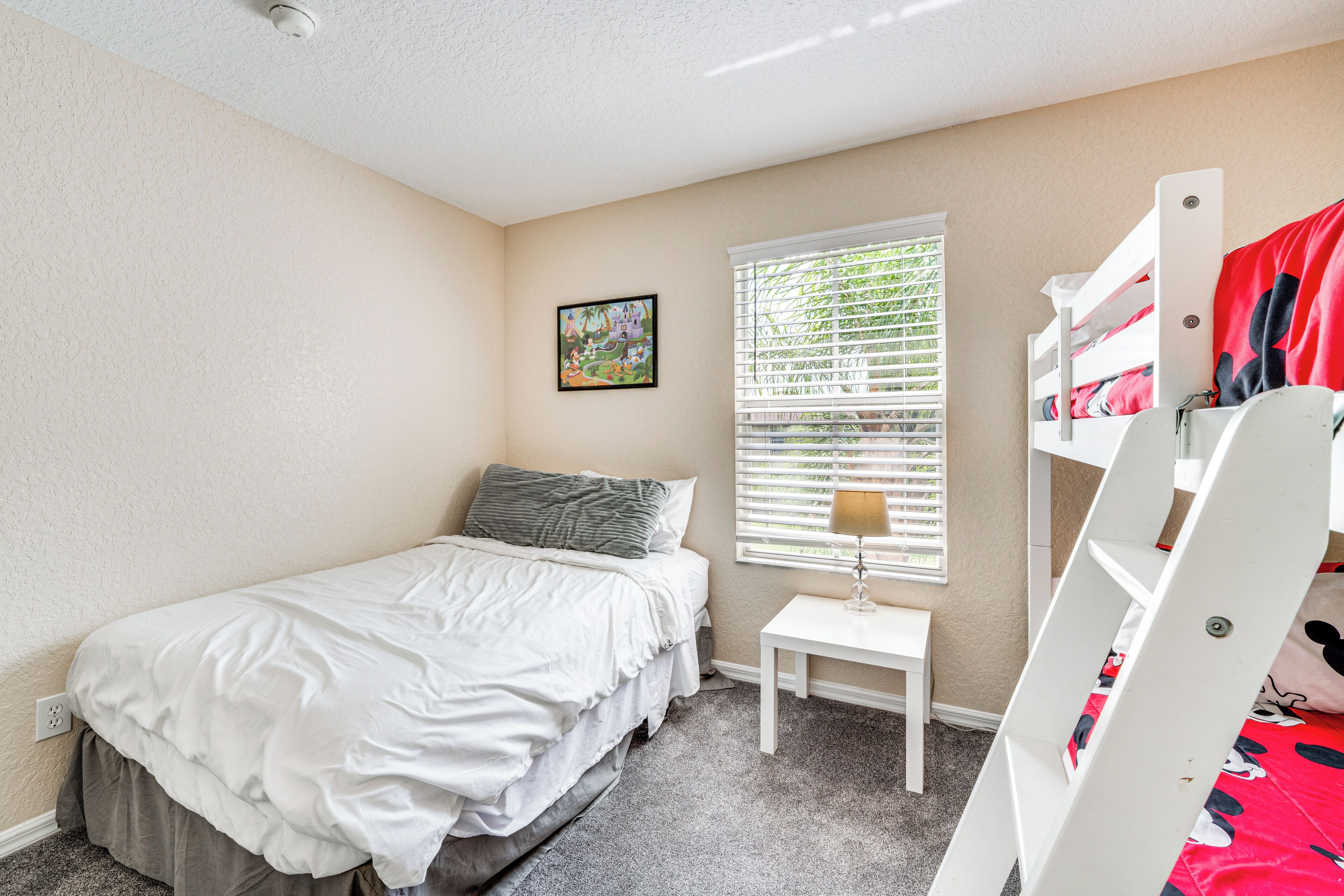 Une chambre avec un lit superposé, une petite table de chevet, une fenêtre avec des stores et un lit simple avec un oreiller.