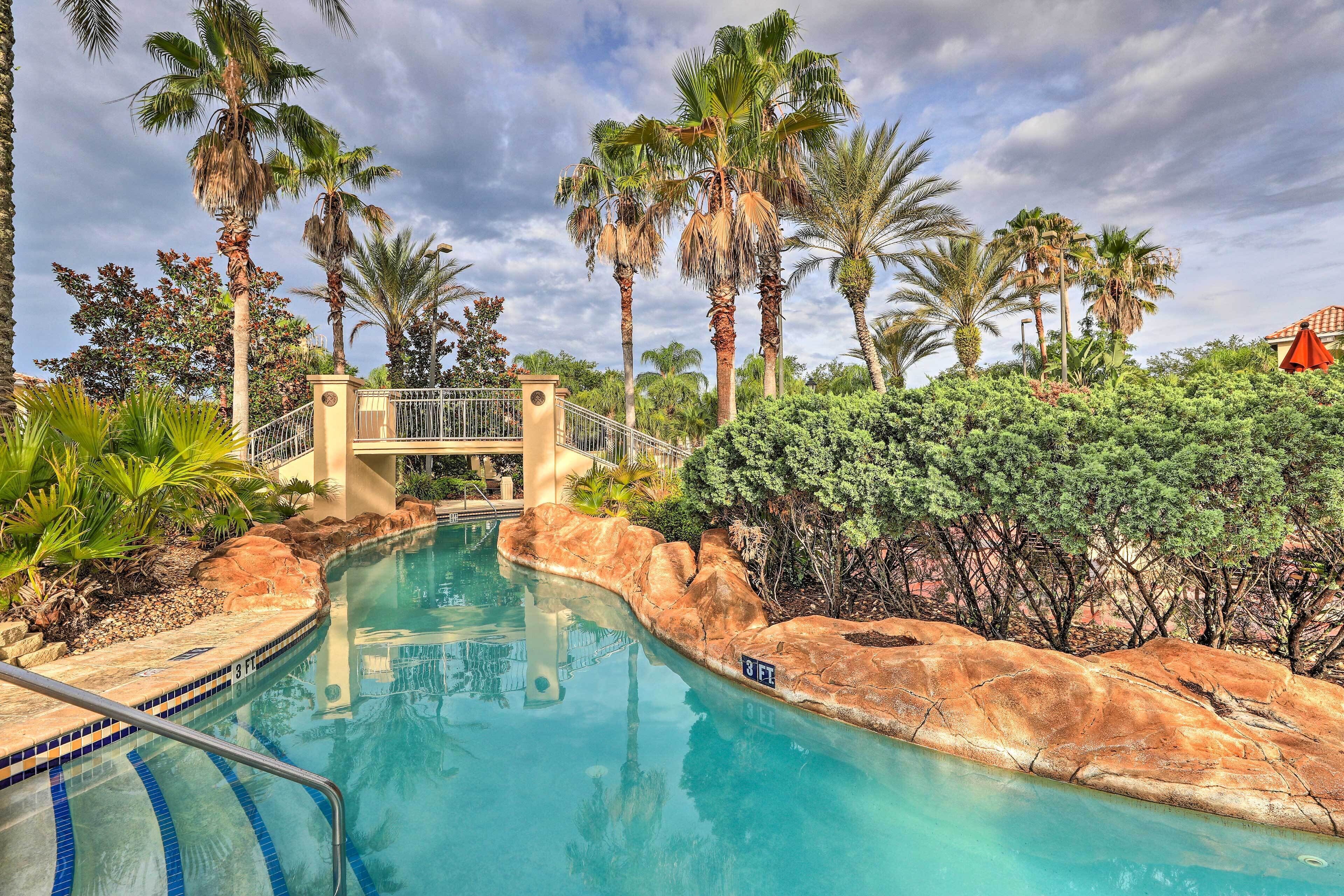 A swimming pool with a bridge, surrounded by palm trees and a rocky landscape.